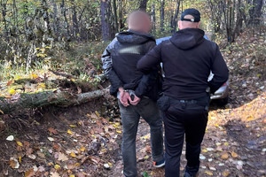 Na zdjęciu widać policjanta oraz zatrzymanego mężczyznę prowadzonego przez las.