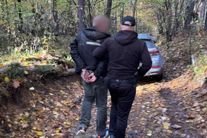 Na zdjęciu widać policjanta oraz zatrzymanego mężczyznę prowadzonego przez las.