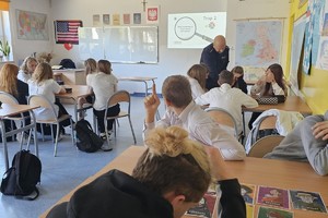 Na zdjęciu widać policjanta oraz uczniów w czasie zajęć w sali lekcyjnej.