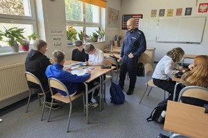 Na zdjęciu widać policjanta oraz uczniów w czasie zajęć w sali lekcyjnej.
