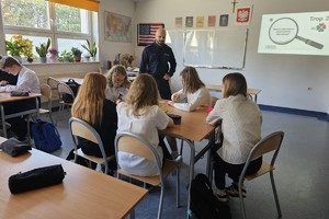 Na zdjęciu widać policjanta oraz uczniów w czasie zajęć w sali lekcyjnej.