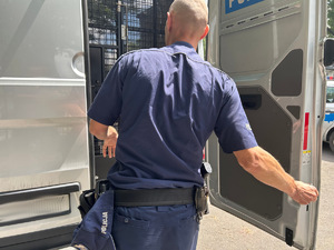 Na zdjęciu widać policjanta oraz samochód służący do przewozu zatrzymanych.