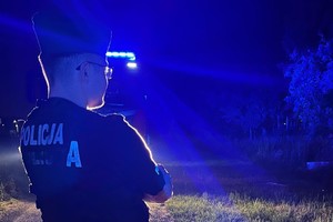 Na zdjęciu widać policjanta i łunę niebieskiego światła radiowozu.