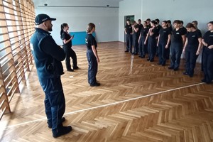 Na zdjęciu widać policjanta i uczniów podczas zajęć z musztry.