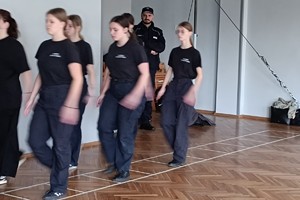 Na zdjęciu widać policjanta i uczniów podczas zajęć z musztry.