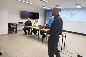 Na zdjęciu widać policjantów, przedstawicielkę sanepidu oraz zgromadzonych uczniów.