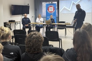 Na zdjęciu widać policjantów, przedstawicielkę sanepidu oraz zgromadzonych uczniów.