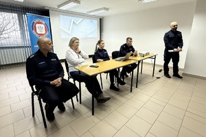 Na zdjęciu widać policjantów, przedstawicielkę sanepidu oraz zgromadzonych uczniów.