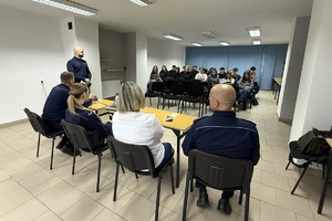 Na zdjęciu widać policjantów, przedstawicielkę sanepidu oraz zgromadzonych uczniów.