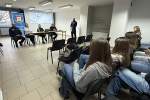 Na zdjęciu widać policjantów, przedstawicielkę sanepidu oraz zgromadzonych uczniów.