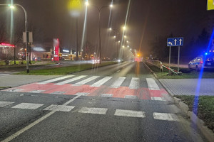 Na zdjęciu widać miejsce zdarzenia drogowego, uszkodzony rower oraz bariery drogowe. W tle widać przejście dla pieszych i przejazd dla rowerzystów.