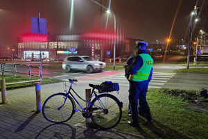 Na zdjęciu widać miejsce zdarzenia drogowego, uszkodzony rower oraz bariery drogowe. W tle widać przejście dla pieszych i przejazd dla rowerzystów.