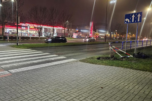 Na zdjęciu widać miejsce zdarzenia drogowego, uszkodzony rower oraz bariery drogowe. W tle widać przejście dla pieszych i przejazd dla rowerzystów.