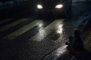 Grafika przedstawia drogę i oznakowane przejście dla pieszych, na które wjechał właśnie samochód, obok przejścia na ziemi ma siedzi chłopiec.