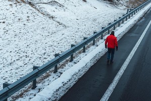 Grafika przedstawia mężczyznę idącego poboczem autostrady, panują zimowe warunki.