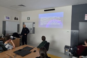Na zdjęciu widać policjanta oraz uczniów w sali lekcyjnej.