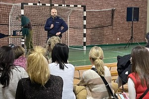 Na zdjęciu widać policjanta i rodziców podczas spotkania w sali gimnastycznej szkoły.