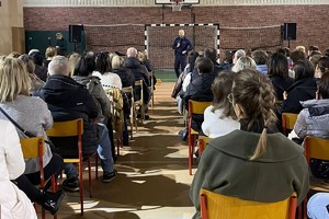 Na zdjęciu widać policjanta i rodziców podczas spotkania w sali gimnastycznej szkoły.