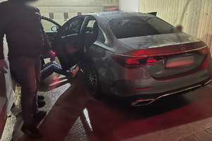 Na zdjęciu widać policjanta, mężczyznę siedzącego na podłodze i szary samochód.