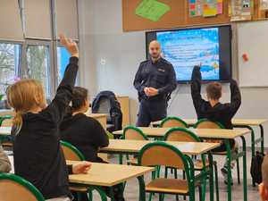 Na zdjęciu widać policjanta i uczniów w sali lekcyjnej.