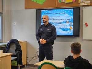 Na zdjęciu widać policjanta i uczniów w sali lekcyjnej.