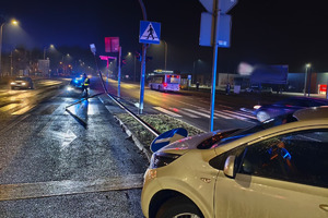 Na miejscy widać radiowóz, uszkodzony biały samochód i miejsce zdarzenia drogowego.
