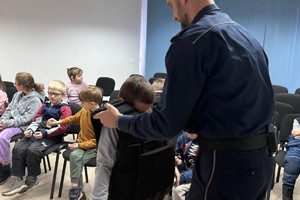 Na zdjęciu widać policjanta oraz przedszkolaki w trakcie profilaktycznych zajęć.