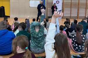 Na zdjęciu widać policjanta, przedstawicielkę sanepidu oraz zgromadzone dzieci.