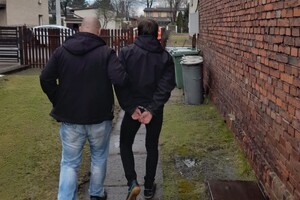 Na zdjęciu widać mężczyznę w kajdankach prowadzonego przez policjanta.