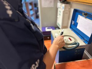 Na zdjęciu widać policjantkę stojącą przed urządzeniem do pomiaru alkoholu w organizmie.