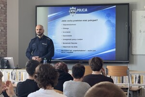 Na zdjęciu widać policjanta i uczniów zgromadzonych w sali.