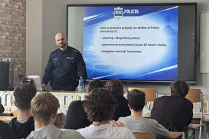 Na zdjęciu widać policjanta i uczniów zgromadzonych w sali.