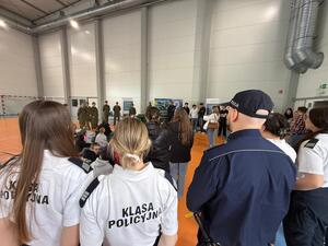 Na zdjęciu widać policjantów, funkcjonariuszkę Straży Granicznej oraz zgromadzonych uczniów.