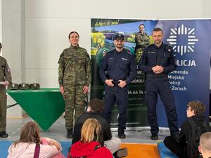 Na zdjęciu widać policjantów, funkcjonariuszkę Straży Granicznej oraz zgromadzonych uczniów.