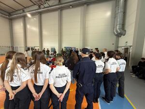 Na zdjęciu widać policjantów, funkcjonariuszkę Straży Granicznej oraz zgromadzonych uczniów.