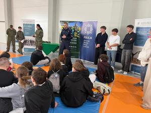 Na zdjęciu widać policjantów, funkcjonariuszkę Straży Granicznej oraz zgromadzonych uczniów.