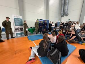 Na zdjęciu widać policjantów, funkcjonariuszkę Straży Granicznej oraz zgromadzonych uczniów.