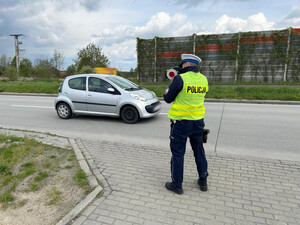 Na zdjęciu widać policjanta podczas pomiaru prędkości oraz przejeżdżający samochód.