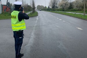 Na zdjęciu widać policjanta i drogę. Policjant wykonuje pomiar prędkości.