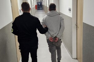 Na zdjęciu widać policjanta, który korytarzem prowadzi zatrzymanego mężczyznę.