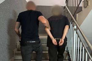 Na zdjęciu widać prowadzonego przez policjanta mężczyznę w kajdankach.