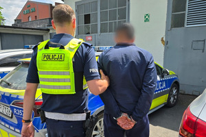 Na zdjęciu widać policjanta, który prowadzi zatrzymanego mężczyznę. W tle widać radiowozy.
