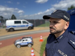 Na zdjęciu widać policjanta, radiowóz oraz uczestników biegu.