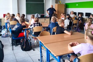 Na zdjęciu widać policjanta oraz uczniów w klasie lekcyjnej.