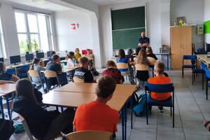 Na zdjęciu widać policjanta oraz uczniów w klasie lekcyjnej.