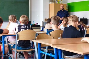 Na zdjęciu widać policjanta oraz uczniów w klasie lekcyjnej.
