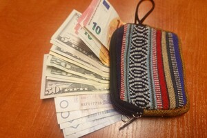 Na zdjęciu widać portfel, z którego wystają pieniądze w różnych walutach.
