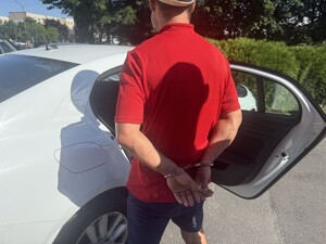 Na zdjęciu widać mężczyznę w kajdankach na tle samochodu.