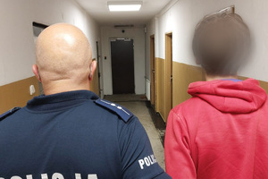 Na zdjęciu widać policjanta oraz mężczyznę w czerwonej koszulce, a w tle korytarz.