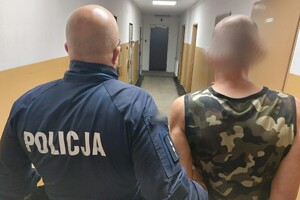 Na zdjęciu widać policjanta i mężczyznę prowadzonego korytarzem.